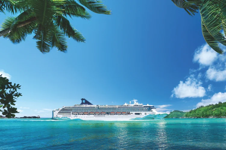 Gemini hat gesagt Ein großes weißes Kreuzfahrtschiff mit bunter Rumpfbemalung liegt auf dem türkisblauen Meer vor einer tropischen Küste mit Palmen.